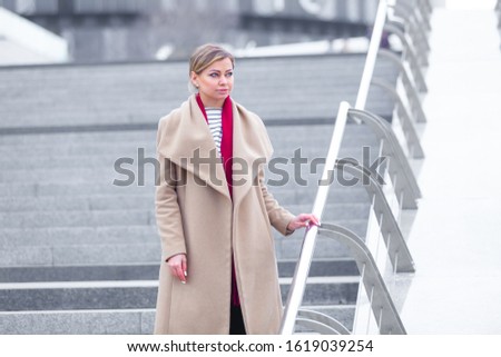 At the mall lifestyle fashion portrait of stunning brunette girl. Walking on At the mall. Going shopping. Wearing stylish white fitted coat, red neckscarf. Business woman. Black bag.