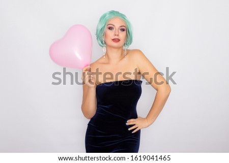 Beautiful young woman with short mint hair standing over white background, holding pink heart balloon