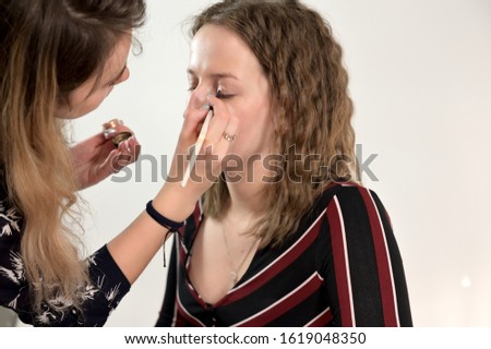 Applying cosmetics. Close-up portrait of a makeup artist doing makeup of a female model in a studio.