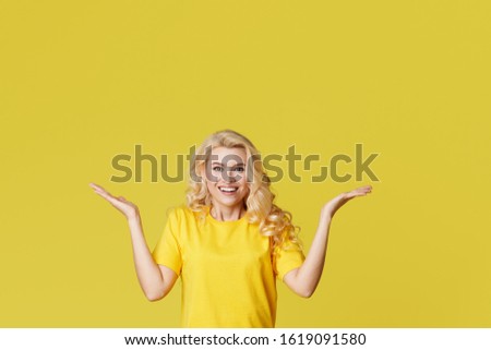 Young happy woman shows hands up, spreads his hands to the sides. Above is an empty place for text and inscription on a yellow background. 