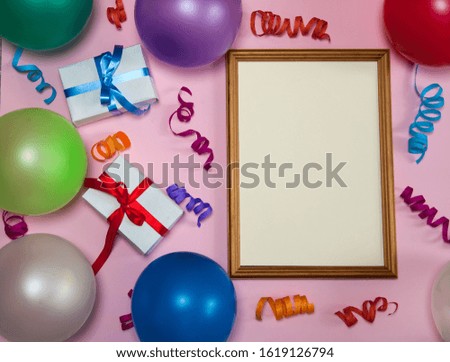 The concept of birthday. Wooden photo frame, multicolored streamer, gift boxes and balloons on a pink background.
