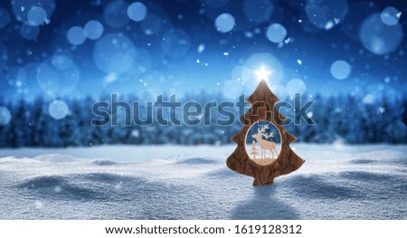 Christmas tree with star in snow and snowflakes in front of a forest in blue color