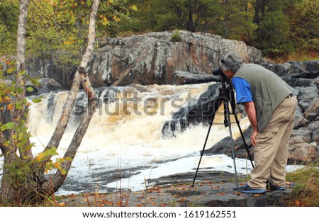 Nature Photographer taking a photo of a Waterfall with Autumn colors in the background