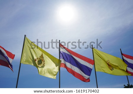 The sun is shining light over Thai national flags and His Majesty King Vajiralongkorn flags.