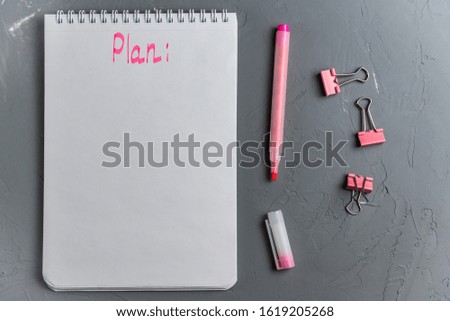 White notebook template on a spring with a pink inscription "plan" on a gray concrete background. Stylish female desktop. Flat lay