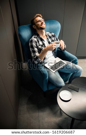 Top view of smiling guy sitting in armchair and enjoying hot drink stock photo