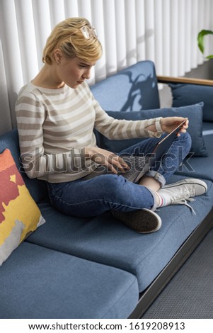 Attractive woman typing on gadget while sitting on sofa stock photo