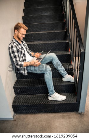 Side view of smiling male freelancer resting on stairs with laptop stock photo