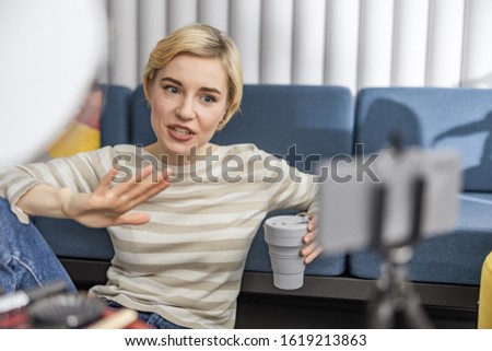 Smiling young woman holding coffee while sitting on floor and making video stock photo
