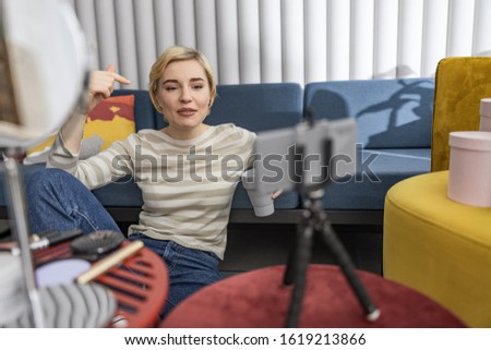 Happy female blogger with hot drink sitting on floor near sofa stock photo