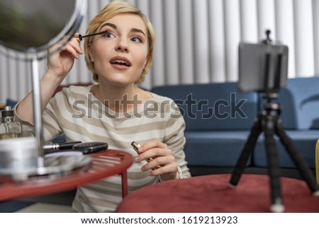 Waist up of attractive woman using mascara while making video stock photo
