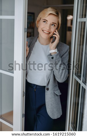 Smiling attractive lady opening the door while holding mobile phone stock photo