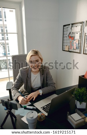 Waist up of smiling beautiful lady making notes at desktop stock photo