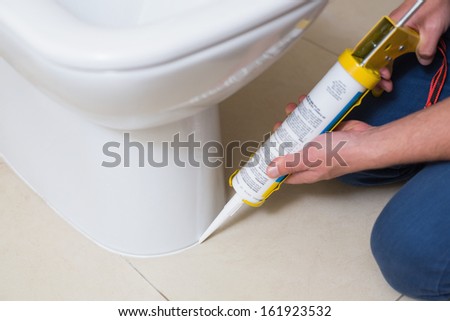 Close up of a plumber fixing toilet in a washroom with silicone cartridge Royalty-Free Stock Photo #161923532
