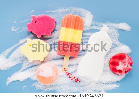 Bottle with washing agent and sponges on soapy foam background. Washing dishes concept. Flat lay, Top view.