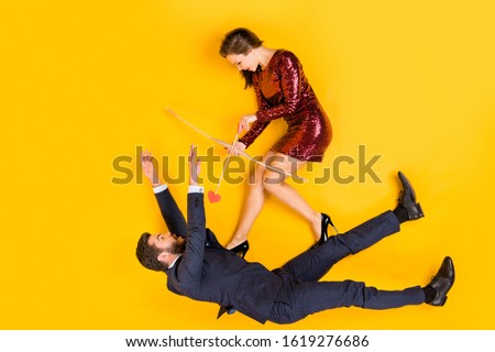 Top above high angle view full body photo of two students people cunning girl shoot aim cupid arrow shocked man fall wear red mini dress tuxedo lay isolated yellow color background