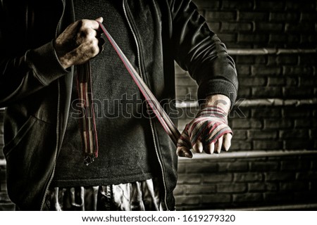 Young boxer preparing for fight, wrapping hands with bandage, copy space. Mixed media