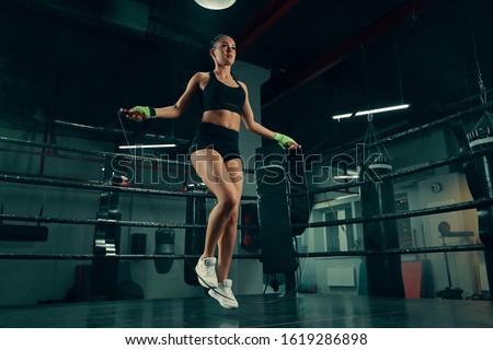 Young athletic woman training with jumping rope on boxing ring wearing fighting bandages Royalty-Free Stock Photo #1619286898