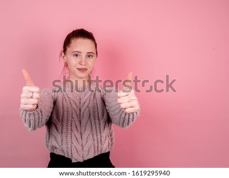 Young woman holding thumbs up on pink background