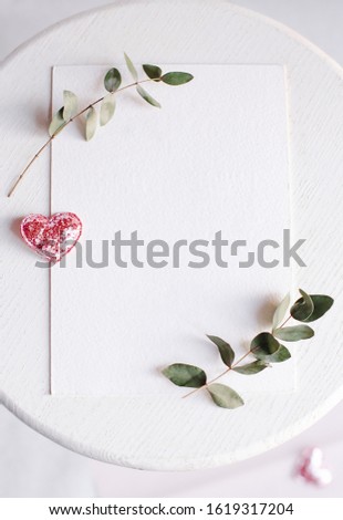 Background with copy space blank on table with glitter heart, eucalyptus branch, flowers and leafs. White paper top view, flat lay, minimal style. Moke up card