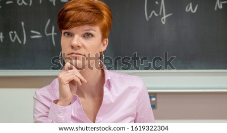 Portrait of young female teacher at school lesson with blackboard in background