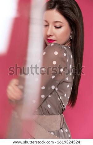 Portrait of beautiful woman with perfect makeup holding glass of champagne with confetti on the vibrant pink background