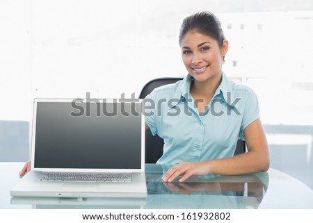 Portrait of an elegant businesswoman displaying laptop on desk in a bright office