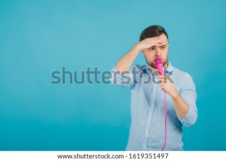 man in blue shirt stands on blue background and sings in pink microphone