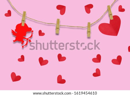 The Valentine's day concept.The red cupid shaped card attached to a wooden clip Hanging with hemp rope on pink background.Valentine's Day background