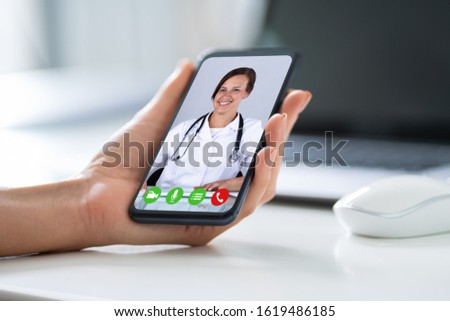Businesswoman's Hand Videoconferencing With Happy Doctor On Smartphone Royalty-Free Stock Photo #1619486185