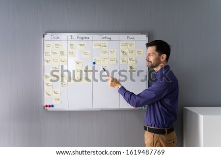 Side View Of Businessman Writing On Sticky Notes Attached To White Board In Office