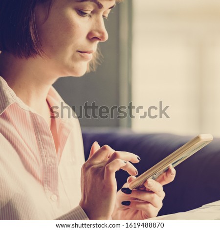 Attractive young woman typing message on smartphone in modern office