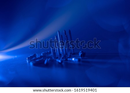 Screws and dowels of different sizes on a white background lit by a blue flash with lens flares showing the screws pointing upwards and the dowels