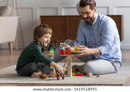 Loving young father sit on floor with cute little son engaged in funny childish activity in living room together, caring dad have fun play with small boy child involved in interesting game at home Royalty-Free Stock Photo #1619558995