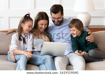Overjoyed young Caucasian family sit rest on couch in living room watch funny video laugh using laptop, excited parents with little kids relax on sofa have fun browse modern computer gadget together