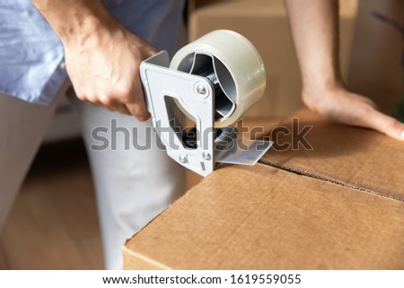 Close up of male renter or tenant packing personal belongings use scotch in carton parcels moving to new home, man hold tape dispenser seal cardboard box package relocating, delivery service concept Royalty-Free Stock Photo #1619559055