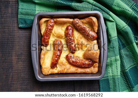 Sunday roast dish toad in a hole of yorkshire pudding with roasted sausages served on dark rustic wooden background  view from above, close up, copy space 