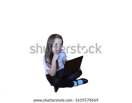 a little schoolgirl girl on a white isolated background is studying and playing on a laptop at home on the floor