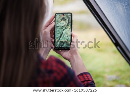 Women hands holding smartphone with app navigation hiking map on screen.  Mountains map with route and markers. Girl planning a trip inside the tent at the camp.  Royalty-Free Stock Photo #1619587225