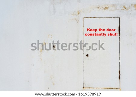 Old metal door in the wall painted with white paint with the inscription "Keep the door constantly shut!"