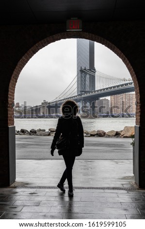 Silhouette of a tourist woman with warm clothes from Dumbo neighborhood with the Manhattan Bridge on the background. Winter season.