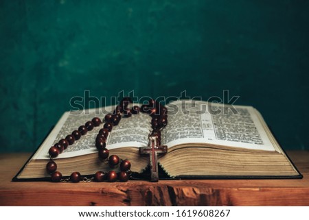 Open Holy Bible and beads crucifix on a red old wooden table. Beautiful green wall background.