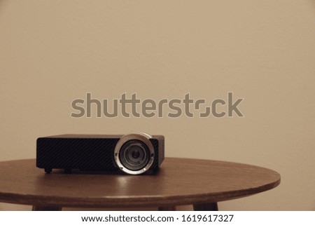 Modern video projector on wooden table against beige background. Space for text