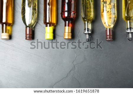 Different sorts of cooking oil in bottles on grey table, flat lay. Space for text