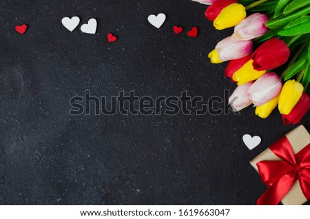 Bouquet of tulips and gift box on dark background. Greeting card for Valentine's Day, Woman's Day and Mother's Day.