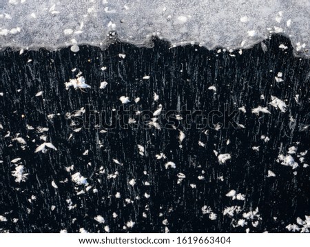 High contrast winter image of clear ice, black ice, lake ice with patterns of snow and  bubbles with space for text or graphics