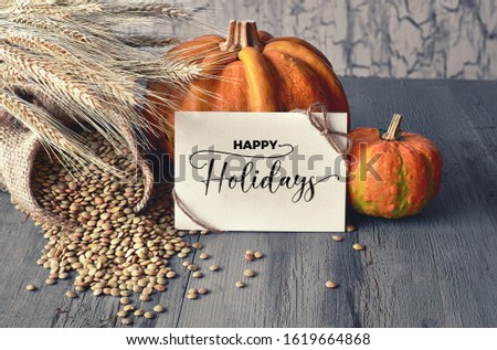 Autumn harvest still life with pumpkins, wheat ears and lentils in sack on faded blue rustic wooden background. Paper card with greeting "Happy Thanksgiving!", toned image.
