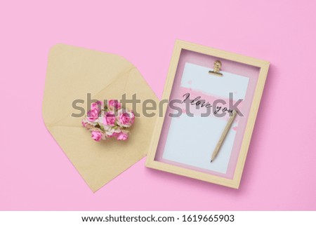 Mockup photo frame with kraft rose flower in brown envelope for Valentines day concept. Top view of mock up photo frame with craft decoration and on pastel pink background. Flat lay with copy space.