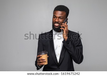 Young african man in suit talking on the phone and drink coffee on gray background