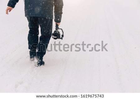 Videographer working in winter during snowfall, cropped photo. Copy space. Professional equipment, camera, stabilizer for video shooting